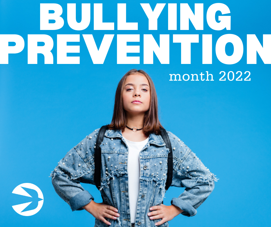 A confident young person stands with hands on hips, wearing a denim jacket and backpack. The text above reads "BULLYING PREVENTION month 2022" in bold white letters. A small white bird logo is in the bottom left corner against a blue background.