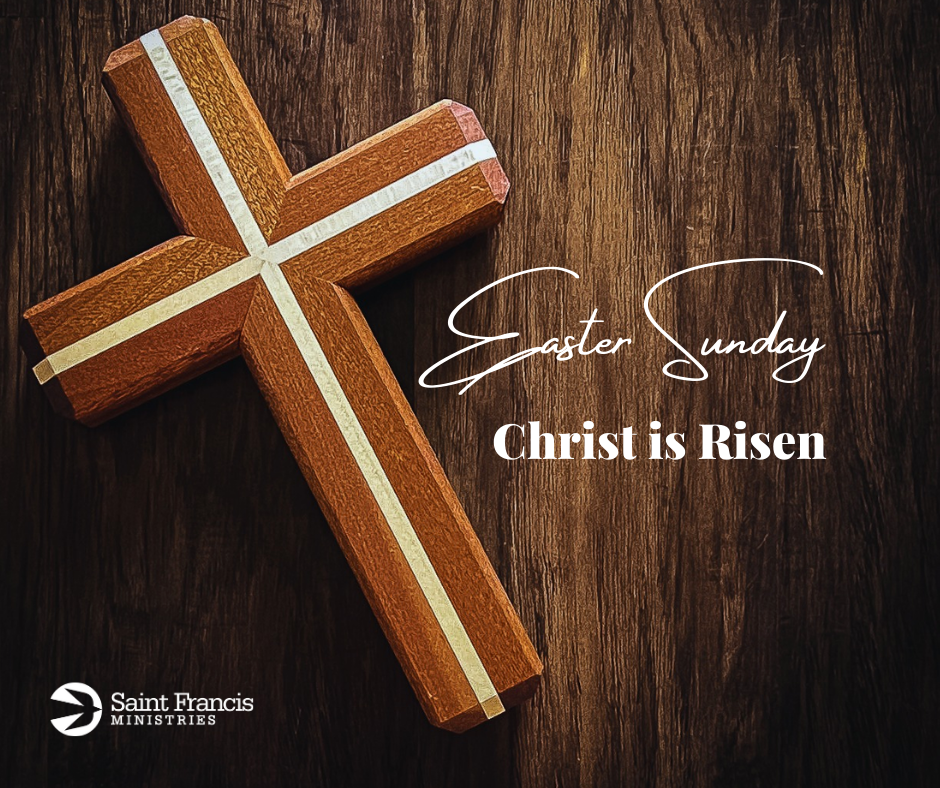 A wooden cross with white stripes is on a dark wood surface. The text reads "Easter Sunday" and "Christ is Risen." The logo of Saint Francis Ministries is in the bottom left corner.