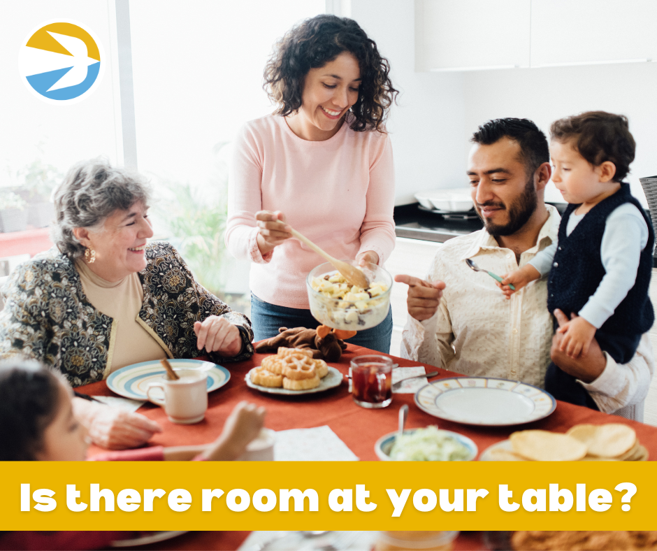 A family of four enjoys a meal together at a dining table. The mother serves food from a bowl, while the father holds a child, and a grandmother smiles. The text on the image reads, "Is there room at your table?" with a blue and yellow logo in the corner.