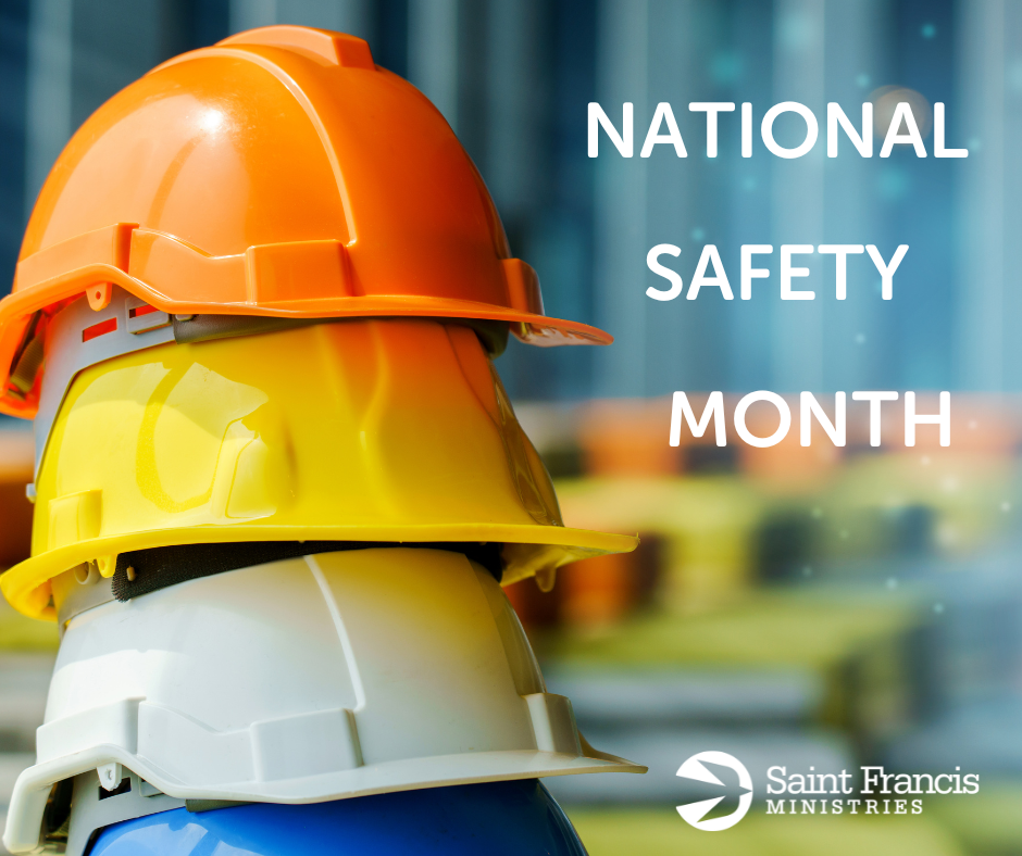 Three construction helmets, colored orange, yellow, and white, stacked on top of each other. The background shows a blurred construction site. The text "National Safety Month" is visible on the right side, along with the Saint Francis Ministries logo at the bottom right.