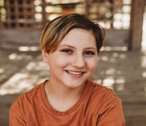 Young girl named Samantha, smiling at the camera, wearing an orange shirt.