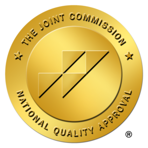 A round gold seal with the text "The Joint Commission National Quality Approval" surrounding a central logo composed of three adjacent parallelograms.