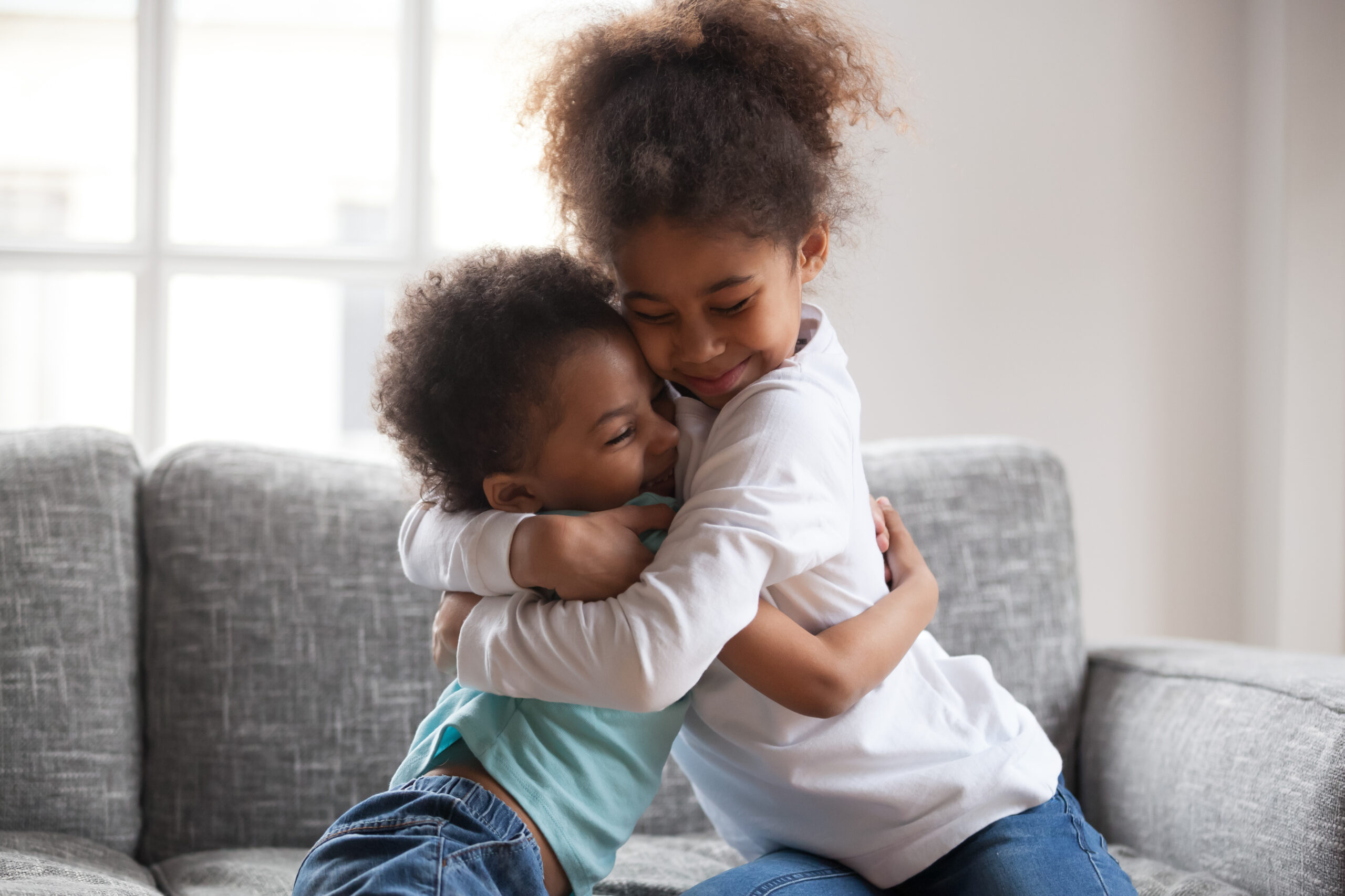 Two young children hugging each other on a couch.