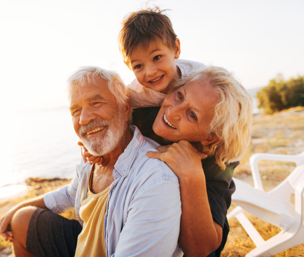 A young boy with his grandparents, smiling on a beach at sunset