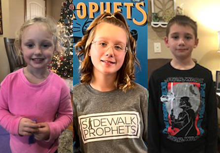 Three children are standing indoors in separate locations. The first child is wearing a pink sweater, the second is wearing a Sidewalk Prophets shirt, and the third is wearing a black Star Wars shirt. They all are smiling or standing calmly.